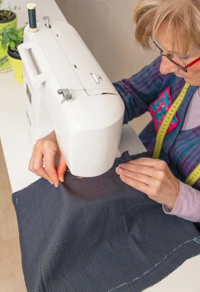 ミシンに取り組んでいるシニア女性の裁縫師女性 — ストック写真