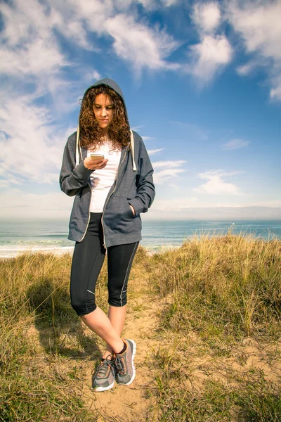 Ung kvinna med hoodie och sportkläder ser smartphone — Stockfoto
