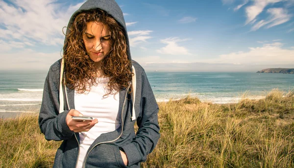 Νεαρή γυναίκα με hoodie και αθλητικών ειδών που ψάχνει το smartphone — Φωτογραφία Αρχείου