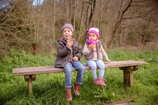 Netter Junge und kleines Mädchen essen Muffins auf Bank sitzend — Stockfoto