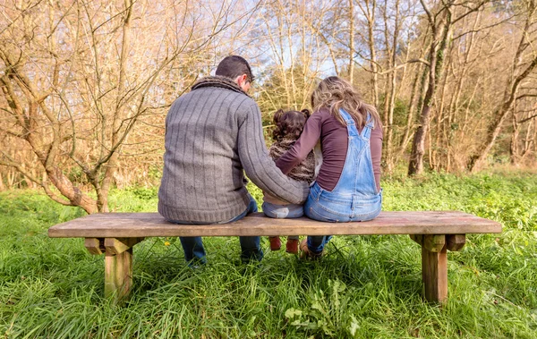 Man and woman hugging little girl sitting on a bench — Stock Photo, Image