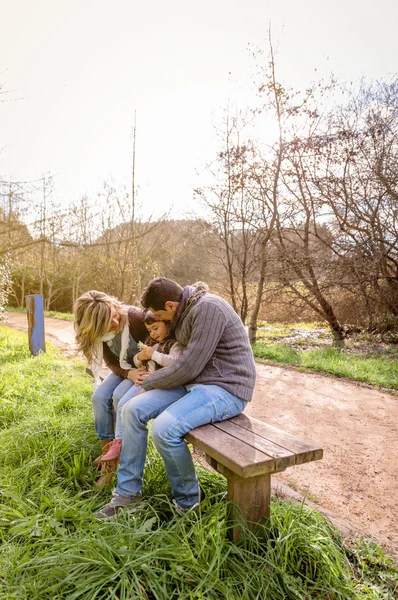 Man and woman playing with little girl sitting on bench — Stock Photo, Image