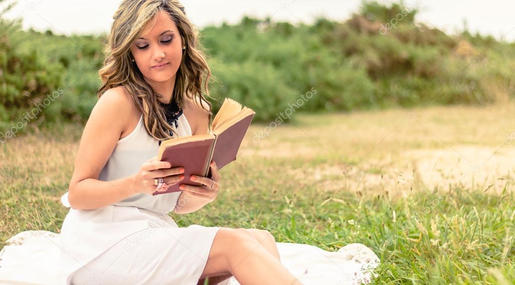 Romantic girl reading a book sitting outdoors