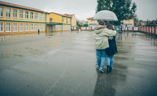 Young couple embracing under umbrella walking in a rainy day — Stock Photo, Image