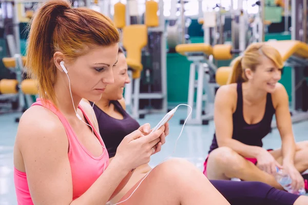 스마트폰 및 체육관에서 얘기 하는 친구 여자 듣기 음악 — 스톡 사진
