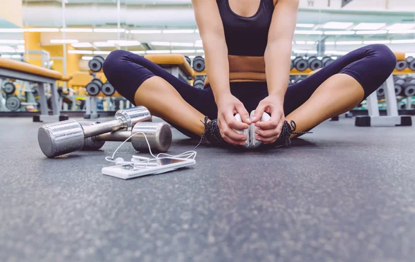 Sporty woman sitting with dumbbells and smartphone in gym floor — Stock Photo, Image