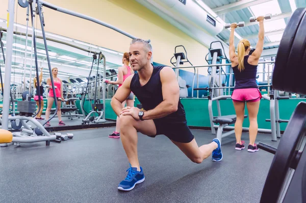 Homme étirement et les femmes faisant haltères exercices dans la salle de gym — Photo