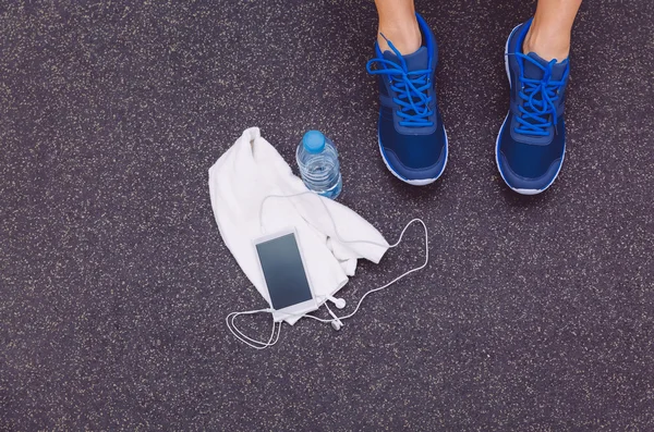 Jambes d'homme avec baskets, serviette, eau et smartphone dans le sol de la salle de gym — Photo