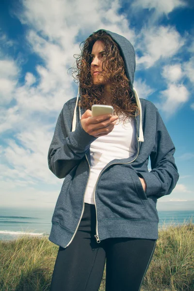 Jovem mulher com capuz e sportswear segurando smartphone — Fotografia de Stock