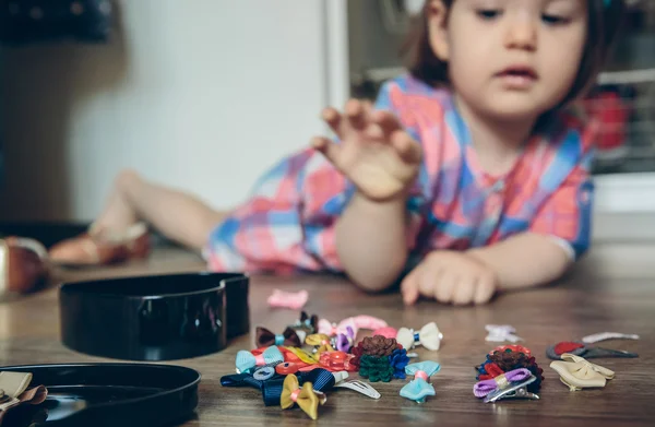 Baby girl playing with hair clips lying in the floor — Stock Photo, Image