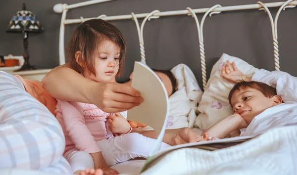 Baby flicka läsa bok med familj i sängen — Stockfoto