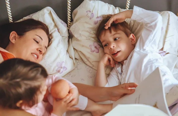 Madre che legge libro ai suoi figli nel letto — Foto Stock