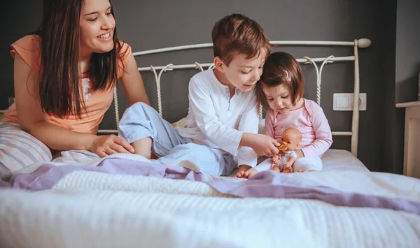 Children feeding doll with cookie sitting over the bed — Stock Photo, Image