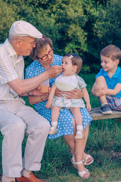 Senior man feeding to baby girl sitting in a bench — Stock Photo, Image