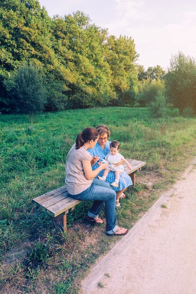 Nő etetése baba lány ül a padon — Stock Fotó