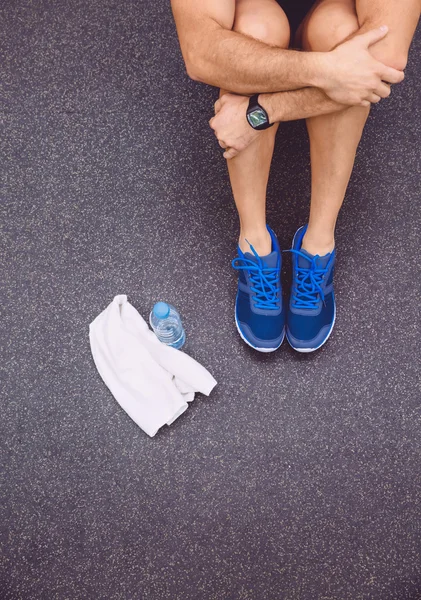 Hombre deportivo sentado con toalla y botella de agua en el suelo del gimnasio — Foto de Stock