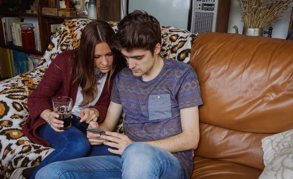 年轻的夫妇看坐在沙发上的智能手机 — 图库照片