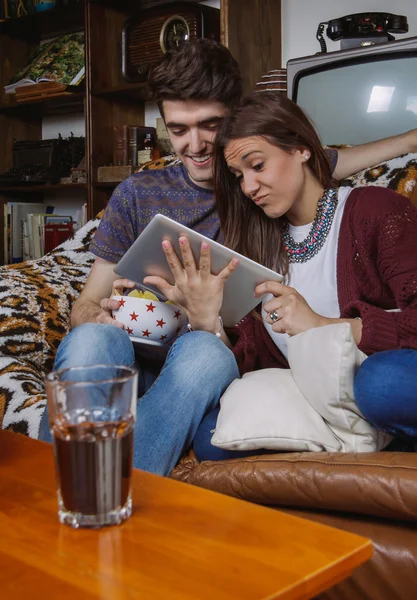 Pareja joven riendo y mirando tableta sentado en el sofá — Foto de Stock