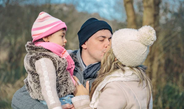 Happy couple with daughter kissing in the forest — Stock Photo, Image