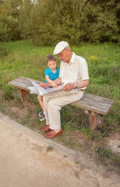Hombre mayor y niño leyendo un periódico al aire libre — Foto de Stock