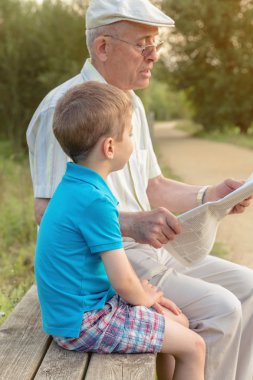 Senior man and child reading a newspaper outdoors clipart