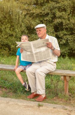 Senior man and bored child reading newspaper outdoors clipart
