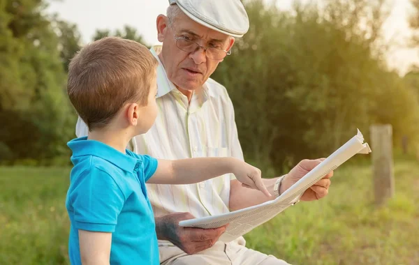 Старший мужчина и ребенок читают газету на улице — стоковое фото