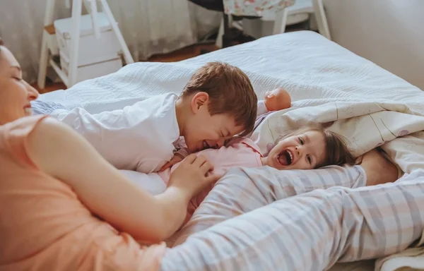 Rahatlamış anne ve oğullar yatağın üzerinde oynuyorlar. — Stok fotoğraf