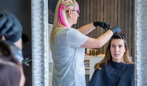 Mujer mirando en el espejo a peluquero peinando el cabello — Foto de Stock