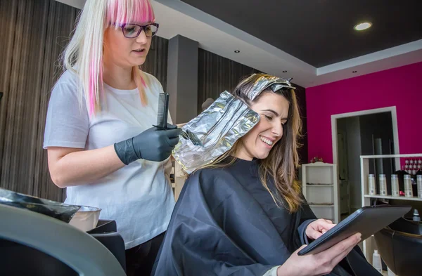 Coiffeur appliquant la teinture capillaire à la femme regardant tablette numérique — Photo