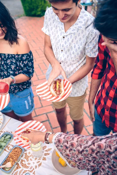 Mladý muž hot dog hospodářství v grilování s přáteli — Stock fotografie