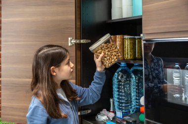 Dolapta depolanmış 72 saatlik hayatta kalma kitine fıstık ekleyen bir kız. Kadın mutfakta acil yemek kileri hazırlıyor, felaketler için. Uyarı, öngörü ve kendi kendine yetme stratejisi.