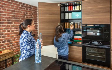 Mutfak kilerinde yiyecek, su ve yiyecek kıtlığı için ilk yardım çantasıyla fıstık saklayan bir kız. Aile 72 saat hayatta kalma kiti hazırlıyor. Öngörü ve kendi kendine yetme stratejisi.