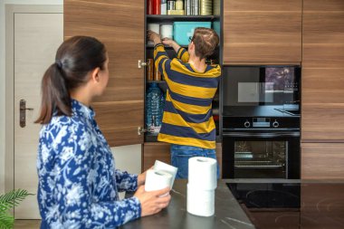 Tanımlanamayan anne ve oğul tuvalet kağıtlarını doldurup mutfakta acil durum kilerine doldurarak potansiyel felaketlere hazırlanıyorlar. 72 saat hayatta kalma çantası konsepti. Öngörü ve kendi kendine yetme stratejisi.