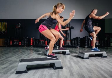 Woman trainer doing aerobic class with steppers in gym clipart