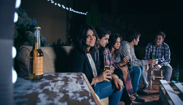 Женщина держит пиво и ее друзья разговаривают на вечеринке — стоковое фото