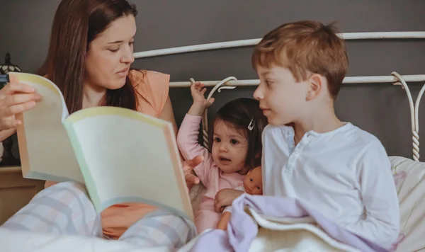 Mor läser bok för sina söner i sängen — Stockfoto