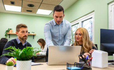 Bir grup profesyonele danışmanlık yapan, bir dizüstü bilgisayara işaret eden ve modern bir çalışma ofisinde yapılan ortak bir toplantıda yeni bir proje stratejisini açıklayan bir işletme koçu.