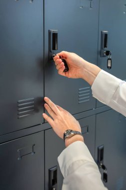 Metal bir ofis dolabında kişisel eşyaları ve iş eşyalarını güvence altına alan tanınmamış bir kadın, modern bir çalışma ortamında iş mahremiyetini, depolamayı ve güvenliği simgeliyor.