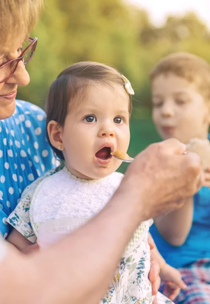 Senior man feeding to baby girl sitting in a bench — Stock Photo, Image