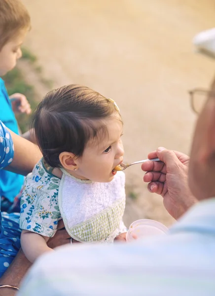 Senior man voeding aan babymeisje, zittend in een bankje — Stockfoto