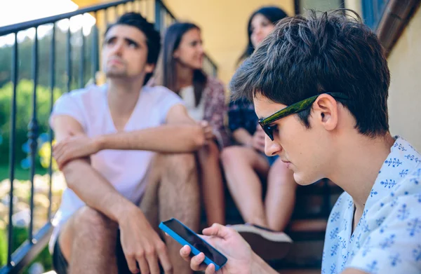 Jovem olhando um smartphone ao ar livre com seus amigos — Fotografia de Stock