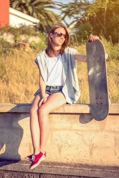 Young girl with skateboard sitting over the wall on summer — Stock Photo, Image