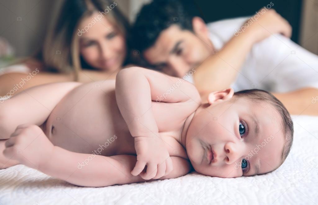 Newborn lying over bed and couple smiling on background