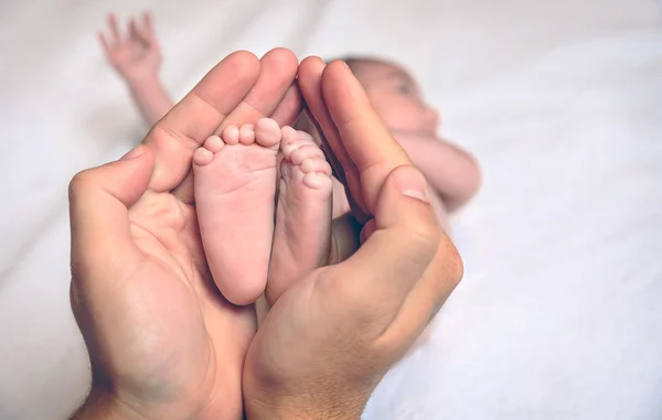 Padre manos sosteniendo los pies del recién nacido acostado sobre la cama —  Fotos de Stock