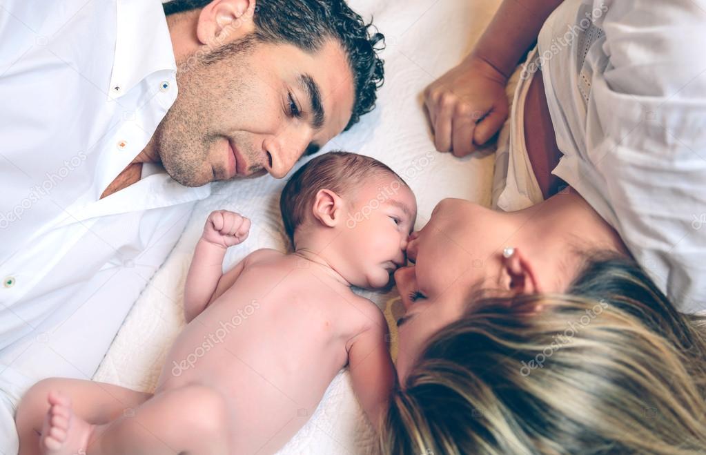 Happy couple lying over bed with their newborn