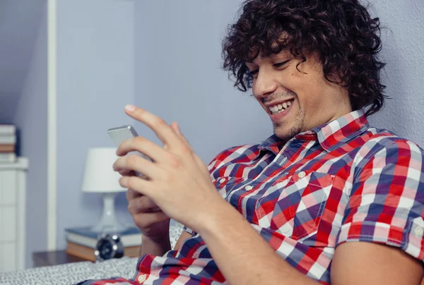 Stilig ung ser smartphone och skrattar — Stockfoto