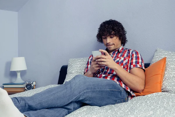 Joven hombre guapo mirando smartphone en una cama — Foto de Stock