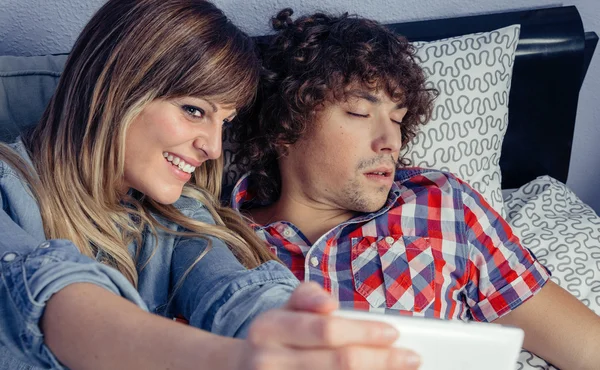 Vrouw nemen foto aan man slapen op bed — Stockfoto