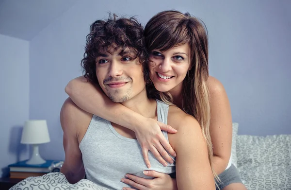 Закохана пара обіймає і посміхається сидячи над ліжком — стокове фото